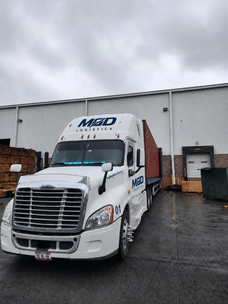 Tractocamión Freightliner Cascadia blanco de MGD, número económico 01, en el andén de una nave bajo la lluvia