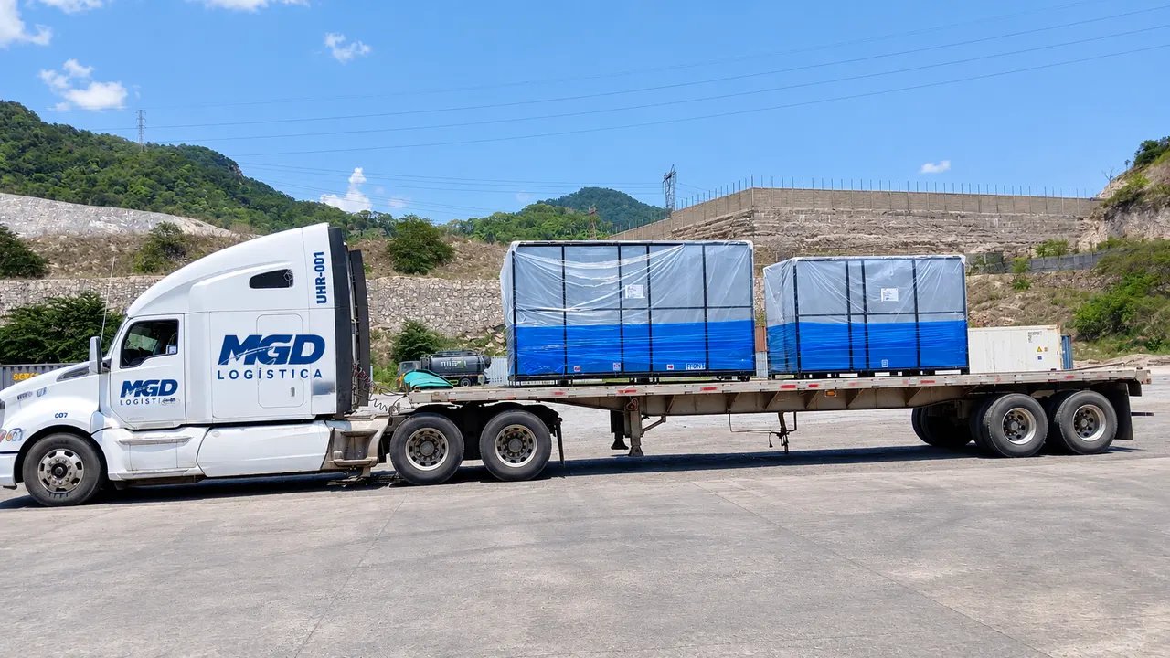 Tractocamión con plataforma cargando dos cajas emplayadas en un patio