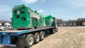 Tractocamión con plataforma de tres ejes cargada con maquinaria emplayada en verde y trincada con bandas