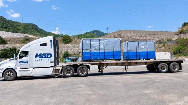 Tractocamión con plataforma cargando dos cajas emplayadas en un patio