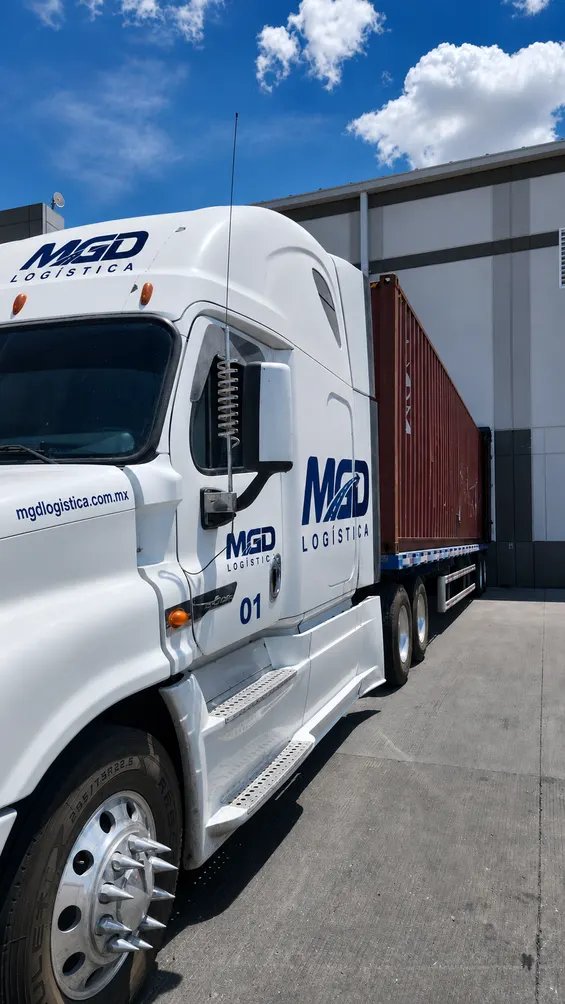 Tractocamión de MGD con un contenedor, visto de lado junto a una nave industrial